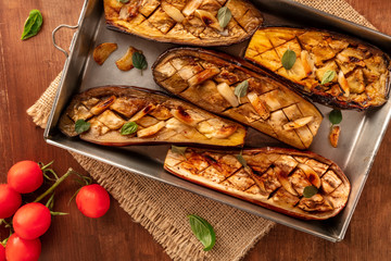 Vegan Italian food. A closeup of baked eggplants with organic cherry tomatoes, garlic, and herbs, shot from above on a wooden background