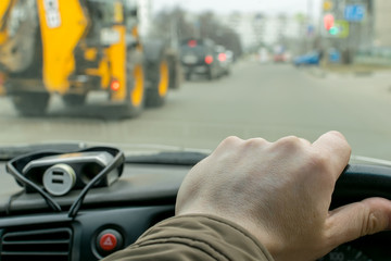 View of the driver's hand on the steering wheel of a car that rides on a city road on the background of a passing tractor nearby