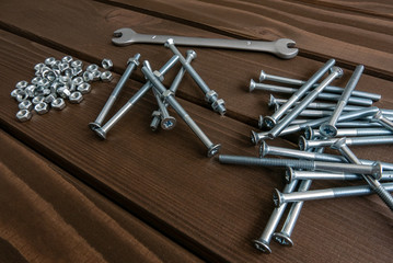 Fototapeta na wymiar Long chrome bolts and nuts lying on wooden planks beside the steel wrench