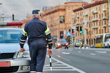 Traffic security officer in blue uniform. Road police man control and prevention of violations on the road. Traffic cop with striped police stick checking and directing trafficc. Police patrol car
