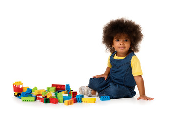 Lovely little cute african american girl on the floor with lots of colorful plastic blocks in studio, isolated