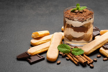 Classic tiramisu dessert in a glass and savoiardi cookies on dark concrete background