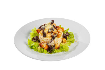 Salad with bread crumbs and prunes on lettuce, carrots, potatoes and mayonnaise on plate, white isolated background, side view