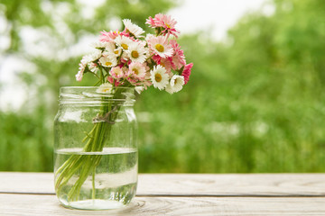 Bouquet of daisies flowers in a glass jar vase in summer on wooden boards in the garden on a green background