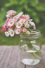 Bouquet of daisies flowers in a glass jar vase in summer on wooden boards in the garden on a green background