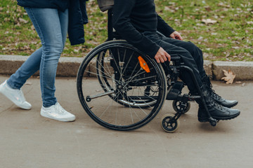 Close-up of a male hand on a wheel of a wheelchair during a walk in the park. Walk together in the park