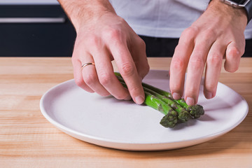 Close-up shot of man's hands laying out steamed green asparagus on the plate,