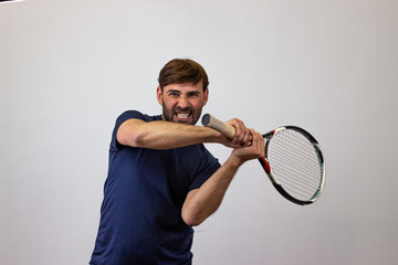Portrait of handsome young man playing tennis holding a racket with brown hair looking euphoric, looking at the camera. Isolated on white background.