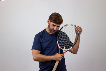 Portrait of handsome young man playing tennis holding a racket with brown hair bored, looking at...