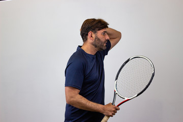Portrait of handsome young man playing tennis holding a racket with brown hair looking overwhelmed,...