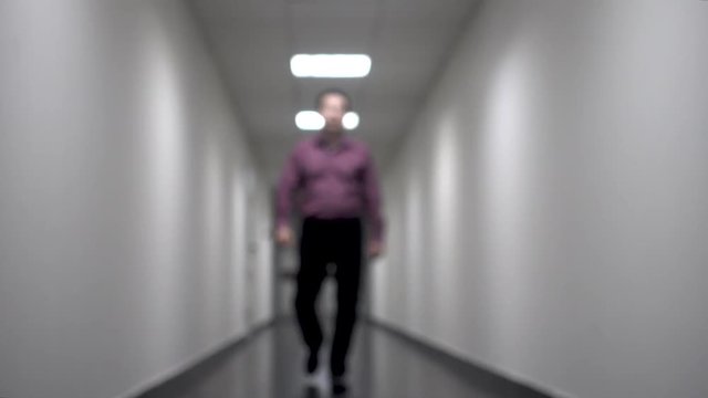 One man walks down the long white corridor. Blurred background. Video contains flicker and noise