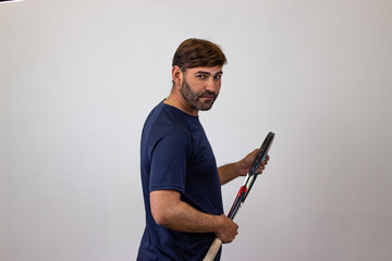 Portrait of handsome young man playing tennis holding a racket with brown hair looking jealous, their back facing the camera and looking at the camera. Isolated on white background.