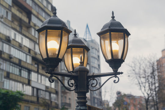Electric light pole lantern on a city street with two bulb lamps and forged metal retro style