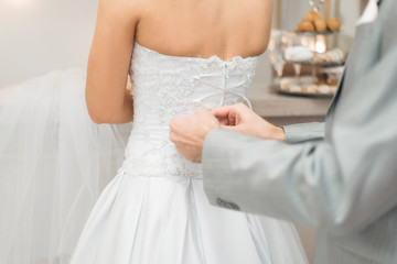 the groom helps his bride to tie the laces on the wedding dress.