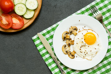 breakfast with fried eggs, mushrooms and vegetables in a white plate on dark background, top view