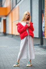 closeup portrait of cute smiling little model girl in red jacket and glasses posing near gray corrugated striped orange gray wall