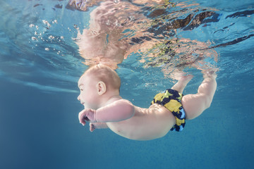 Little baby boy learning to swim underwater in a swimming pool. Healthy family lifestyle and...
