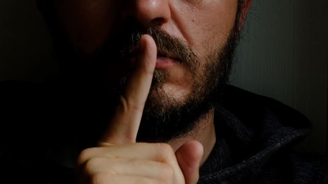 Don't speak, be quiet - close up portrait of bearded man on the door saying shhh. Finger on lips. Head and shoulders, no eyes. Danger. Violence concept.