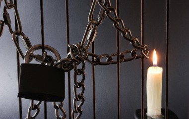 Metal chain, burning candle and padlock on metal fencingn black background