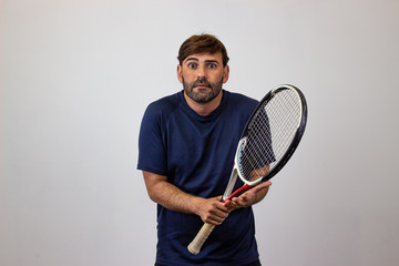 Portrait of handsome young man playing tennis holding a racket with brown hair embarrased, looking at the camera. Isolated on white background.