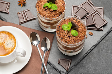 Classic tiramisu dessert in a glass and cup of coffee on dark concrete background
