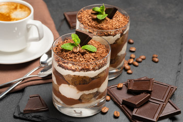 Classic tiramisu dessert in a glass and cup of coffee on dark concrete background