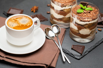 Classic tiramisu dessert in a glass and cup of coffee on dark concrete background