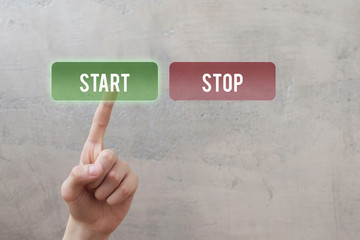 Start stop - finger pressing green translucent start button on virtual touchscreen interface on grunge concrete wall background. Decision making business concept.