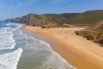 Aerial view of a sandy beach line full of surfers and colorful surfboard on Cordoama beach in Portugal