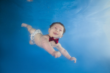 Fototapeta na wymiar Funny face portrait of baby boy with tongue sticking out swimming and diving underwater with fun in the pool. Healthy family lifestyle and children water sports activity. Child development.