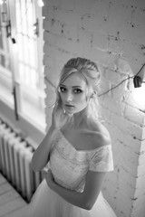 Bride with white dress, with lace top. Hairstyle elegant up-do hair, blonde hair. In a white brick loft-style room.