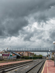 Fototapeta premium Train tracks and pedestrian bridge in the background with a sky of storm clouds in the station of Torrijos, province of Toledo. Castilla la Mancha. Spain