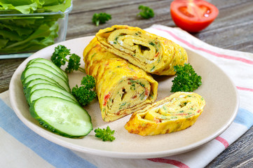Omelette, egg roll with vegetables and herbs on a wooden table. Delicious healthy breakfast.