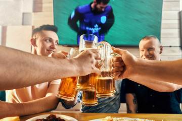 Men keeping glasses of beer and toasting in cafe