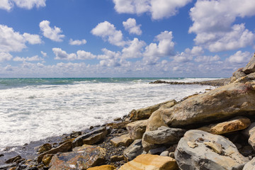 stones on the seashore on the background of sea foam and white clouds in the blue sky