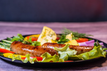 Beautiful grilled sausages on a black plate with vegetables and a background of boards.