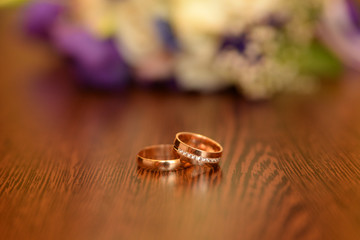 Obraz na płótnie Canvas Beautiful toned picture with wedding rings lie on a wooden surface against the background of a bouquet of flowers
