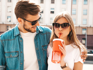 Portrait of smiling beautiful girl and her handsome boyfriend in casual summer clothes. Happy cheerful family having fun on the street background in sunglasses. With bottle of water and straw