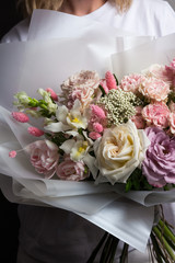 A beautiful wedding bouquet of flowers, fresh roses of different colors, in the hands of a girl, against a gray wall