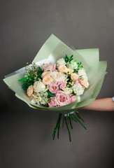 A beautiful wedding bouquet of flowers, fresh roses of different colors, in the hands of a girl, against a gray wall