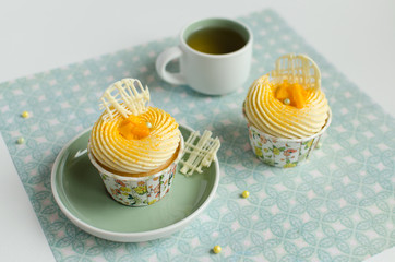 Tropical cupcakes decorated with piece of fresh mango and chocolate elements with a cup of green tea on green background