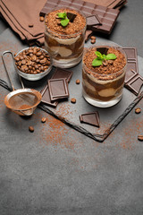 Classic tiramisu dessert in a glass and pieces of chocolate on dark concrete background