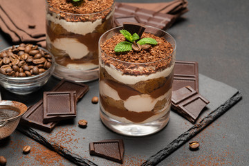 Classic tiramisu dessert in a glass and pieces of chocolate on dark concrete background