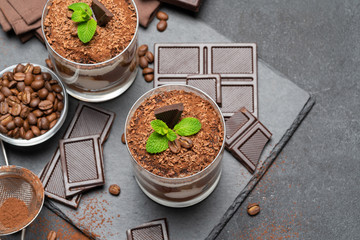 Classic tiramisu dessert in a glass and pieces of chocolate on dark concrete background