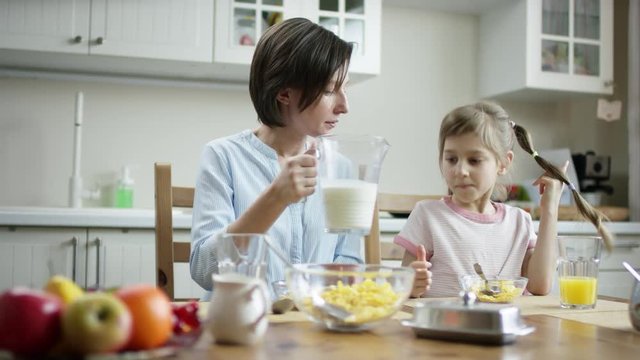 mother add milk to bowl full of cornflakes for her daughter