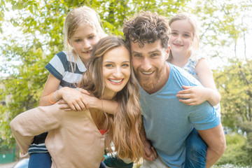 Fototapeta premium Family of four having fun and parents carrying the kids piggyback