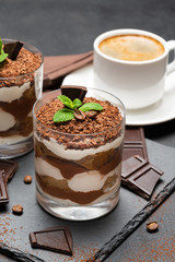 Classic tiramisu dessert in a glass and cup of coffee on dark concrete background