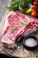 Raw T-bone Steak with fresh herbs and oil on dark wooden background