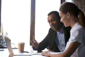 Diverse female male coworkers sitting at desk brainstorming together