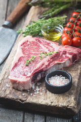 Raw T-bone Steak with fresh herbs and oil on dark wooden background